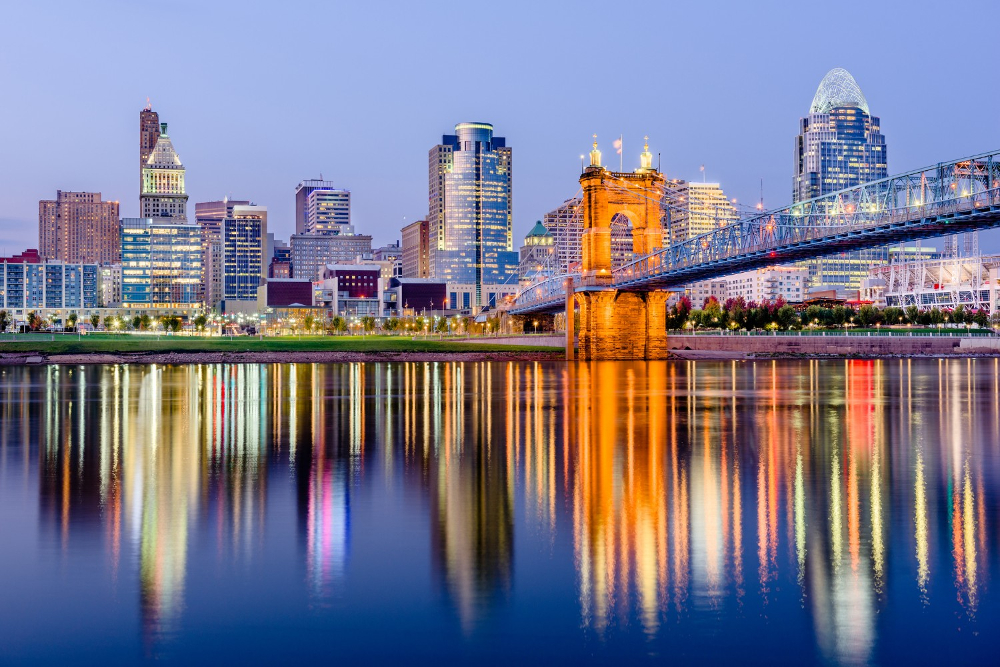 Cincinnati Ohio | Rollins Insurance Night city skyline with a lit bridge over calm river, reflections glowing in the water