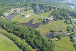 Aerial view of a rural area with winding ponds, green fields, and clusters of trees and buildings.