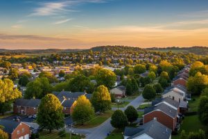 Aerial view of a suburban neighborhood with tree-lined streets and rows of houses at sunset, golden skies overhead.