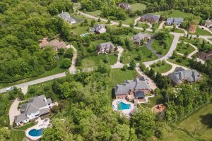 Aerial view of a suburban neighborhood with winding streets, green lawns, and several houses with in-ground pools.