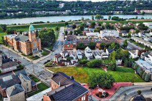 Aerial view of a small riverside town, highlighting a red-brick church, streets, and cluster of houses with green spaces nearby.